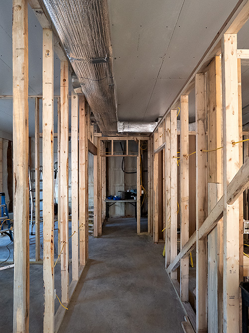 Insulated metal hvac ducts in the ceiling of an unfinished hallway in a building under construction.