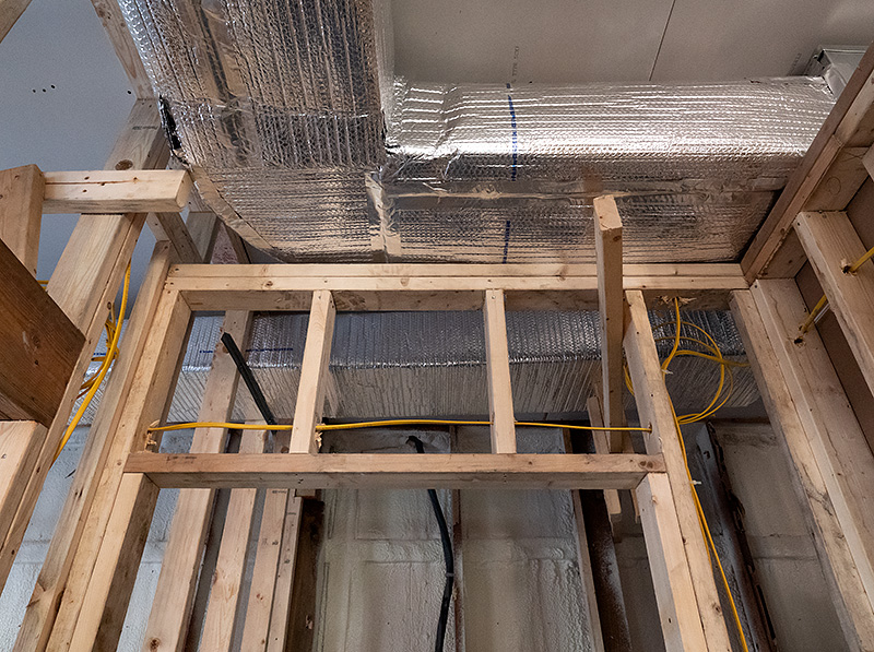 Insulated metal ductwork above the bare wooden wall frames in a new building under construction.