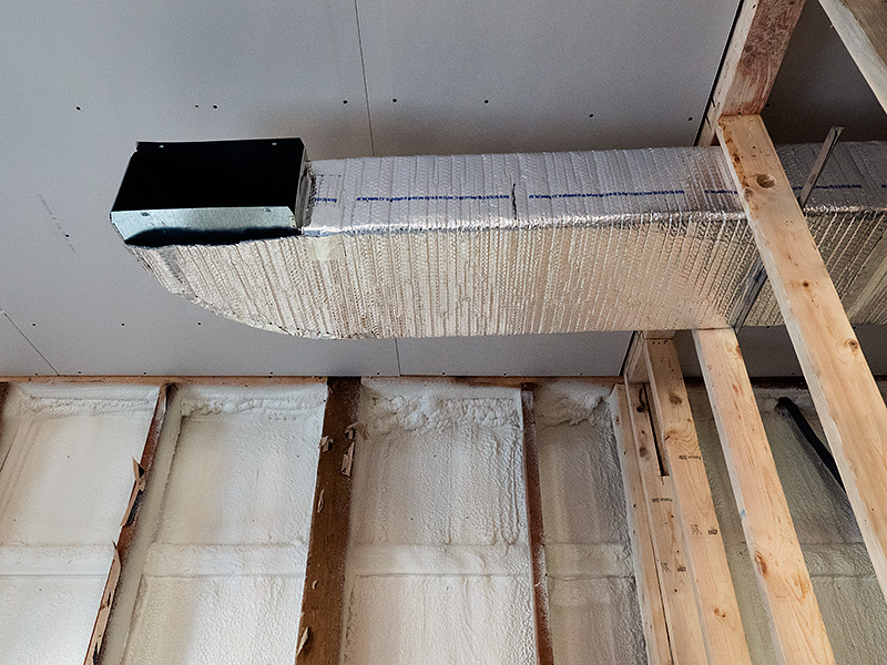 Metal HVAC duct running through the wooden frame of a wall in a building that is being built.