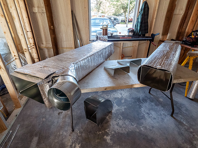 Two metal ducts, wrapped in bubble-wrap insulation, sit on a table awaiting installation in a building that is under construction.